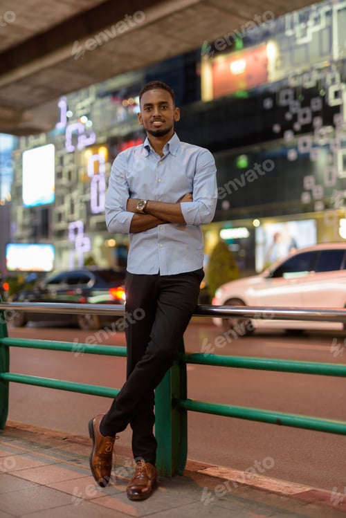 Preview: Full length portrait of handsome black African businessman outdoors in city at night