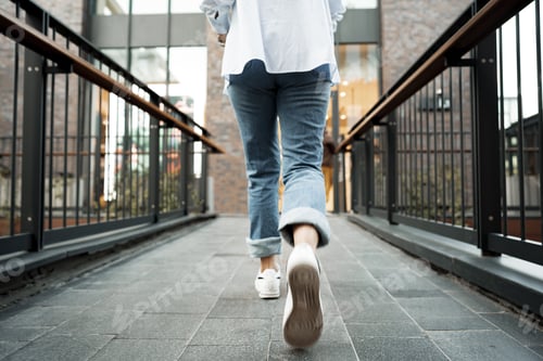 Preview: Back view of a woman in jeans and sneakers walking in the street