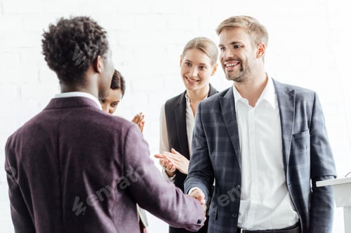 Preview: four multiethnic colleagues in formal wear talking and shaking hands