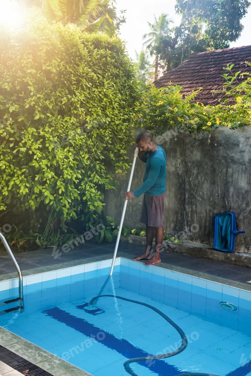Preview: Cleaner man cleaning swimming pool of fallen leaves with with vacuum equipment on backyard