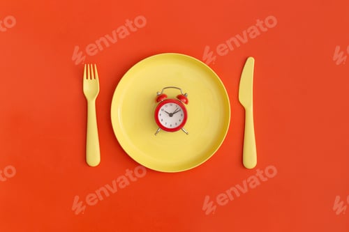 Preview: Red clock on the yellow plate with fork and spoon on a red background. Top view. Flat lay.