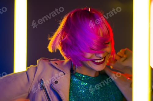 Preview: Amazing smiling woman with dyed pink hairstyle dancing on led-colorful neon lamps background.
