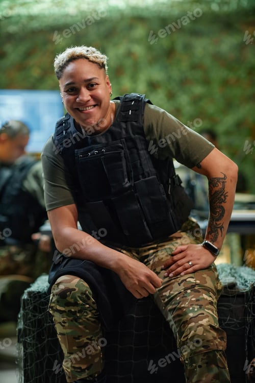 Preview: Smiling multiethnic female officer in body armor sitting on wooden chest