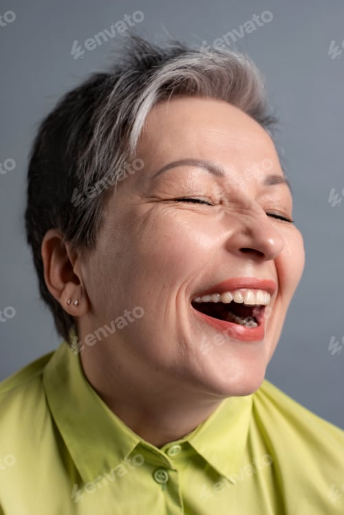 Preview: cheerful funny 50s elderly woman with short gray hair laughing loudly on grey background