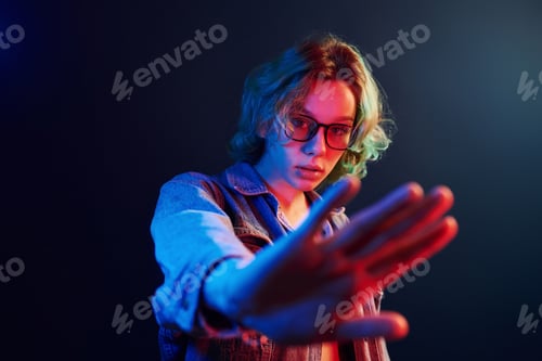 Preview: Portrait of young alternative girl in glasses with green hair in red and blue neon light in studio