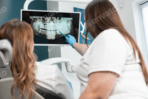 Preview: A female dentist attentively conducts a consultation, showing the patient a panoramic X-ray on the
