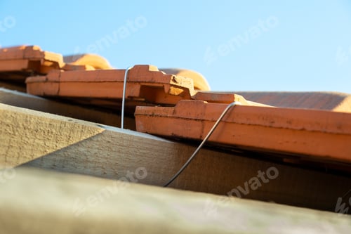 Preview: Closeup of metal montage anchor for installation of yellow ceramic roofing tiles mounted on wooden