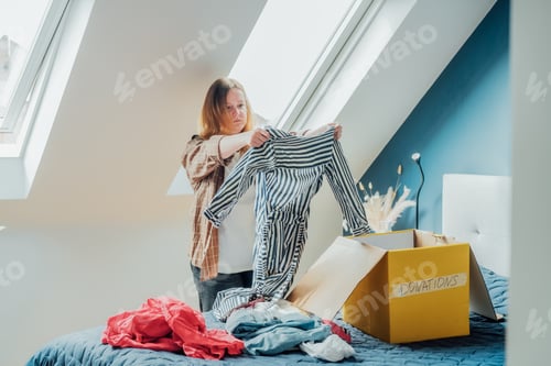 Preview: Woman selecting clothes from her wardrobe for recycling, donating to a Charity shop. Decluttering,