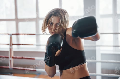 Preview: Shadow fighting. Female sportswoman training in the boxing ring. In black colored clothes