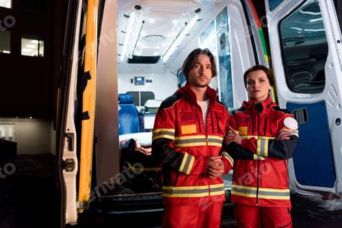 Preview: Tired paramedics in red uniform standing near ambulance car