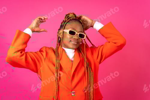 Preview: African young woman with braids on a pink background, in a red suit having fun and dancing