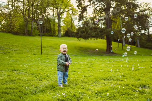 Preview: Little 2 year old boy running on green grass with soap bubbles. Toddler boy enjoying a walk in