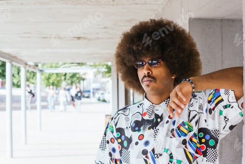 Preview: young black guy with afro hair in white shirt leaning on a concrete wall