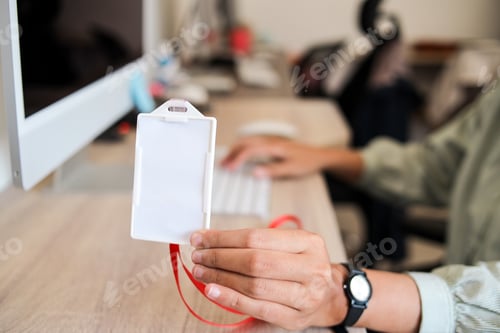 Preview: Person At A Computer Holds A Blank White ID Card With A Red Lanyard, Ready For A Custom Design