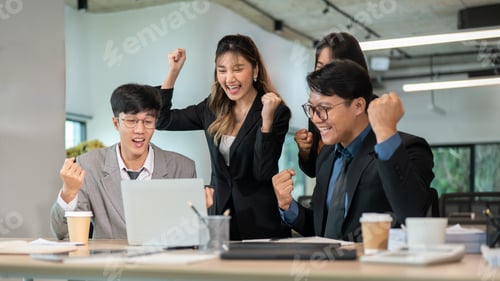 Preview: Smiling businessman and woman raising fist in excited as looking at laptop on wooden table in office