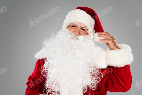 Preview: Santa claus in costume touching hat and looking at camera isolated on grey