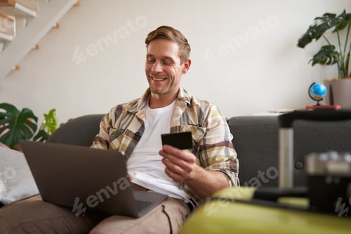 Preview: Happy man booking holiday online on laptop, paying for vacation on travel agency website, buying