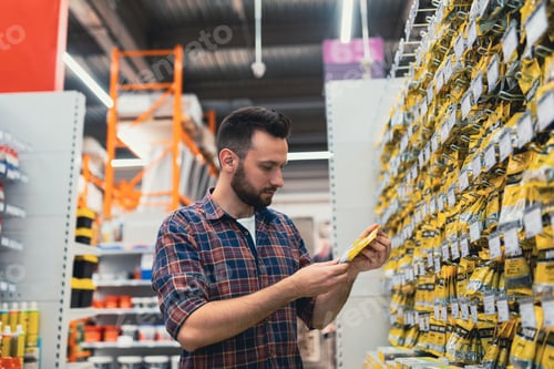 Preview: a man chooses a product in a building materials store next to a showcase with self-tapping screws