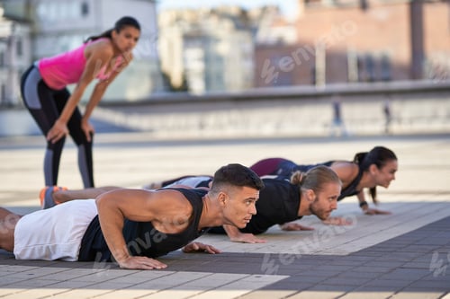 Preview: Young fitness men and women doing push-ups in the city