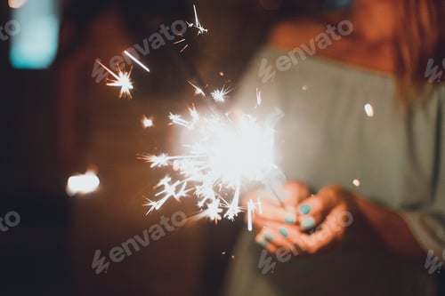 Preview: Young woman holding sparkler in her hands