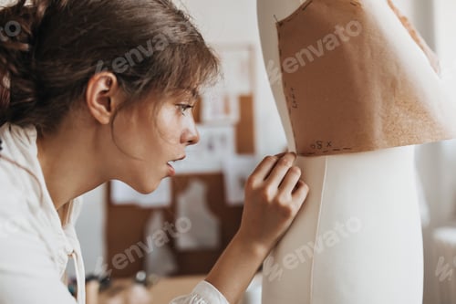 Preview: Brunette woman in white blouse creates clothes pattern. Excited lady in shirt designs new garments