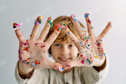 Preview: Smiling boy showing palms with stuck colorful confetti