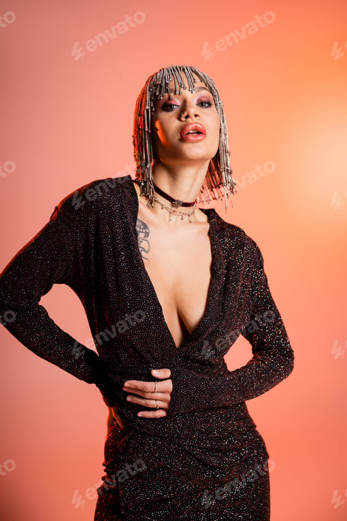 Preview: seductive woman with sexy body posing in jewelry wig and black lurex dress on coral pink background