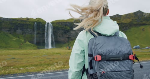 Preview: Woman with backpack walks towards the famous Seljalandsfoss waterfall Iceland