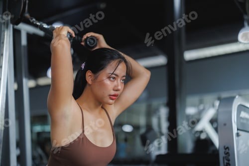 Preview: Determined asian woman performing triceps pushdown exercise in gym