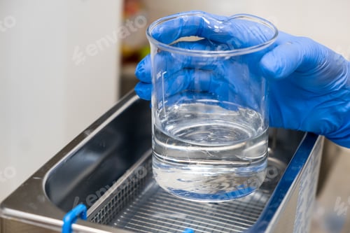 Preview: Scientist in blue rubber puts a beaker for dissolving or cleaning into an ultrasound bath. Clinical