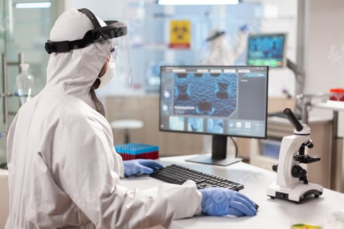 Preview: Medical scientist in ppe suit working with DNA scan image typing on pc