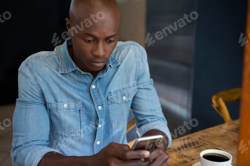 Preview: Man using mobile phone at wooden table in coffee house