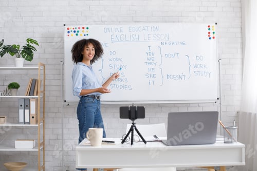 Preview: Smiling african american teacher points to white board with rules and records video for students in