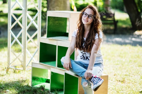 Preview: Portrait of a fashionably dressed girl posing on wooden boxes in the park on a sunny day