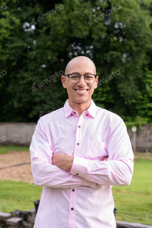 Preview: Happy bald Hispanic man wearing pink casual business shirt and eyeglasses outdoors