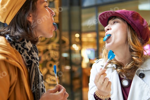 Preview: Happy women joking with blue tongue lollipops