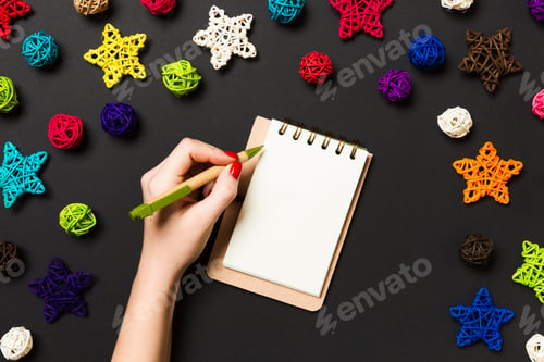Preview: Top view of female hand making some notes in noteebok on colorful background.