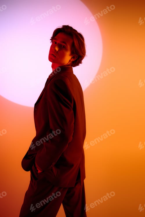 Preview: Young stylish man poses confidently against a vibrant backdrop at twilight