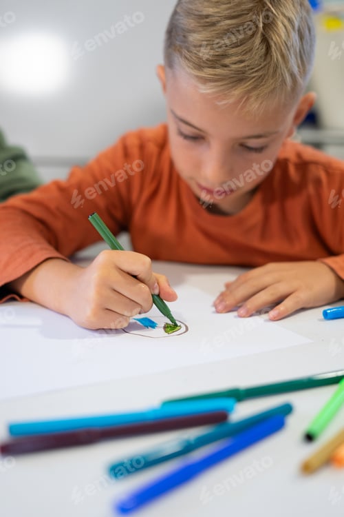 Preview: Young boy drawing with markers at school desk: concentrated child enjoying art class