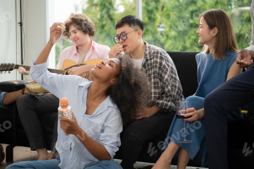 Preview: Group of multiethnic friends having fun at party by playing guitar and singing together at home.