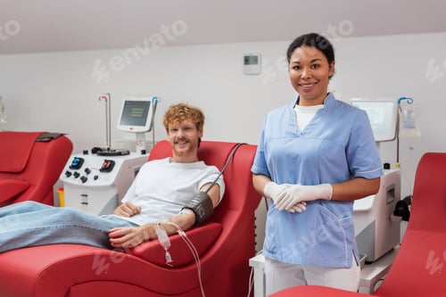 Preview: redhead volunteer with blood pressure cuff and transfusion set smiling at camera near multiracial