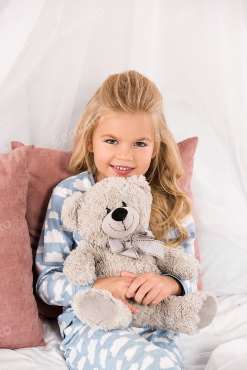 Preview: cheerful cute kid embracing teddy bear in bed