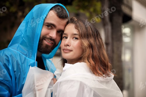 Preview: Young couple in raincoats enjoying time together on city street