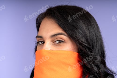 Preview: Woman covering her face with orange scarf on purple background