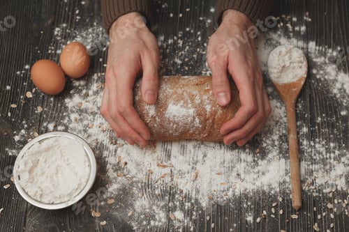 Preview: Close-up of men's hands on black bread with flour powder. Baking and patisserie concept.