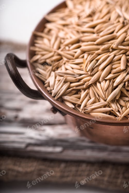 Preview: Oats in a copper bowl on a wooden stand closeup