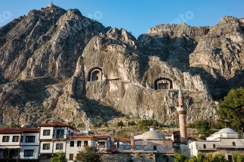 Preview: Ancient rock-cut tombs carved in cliff face above Amasya city with traditional Ottoman houses