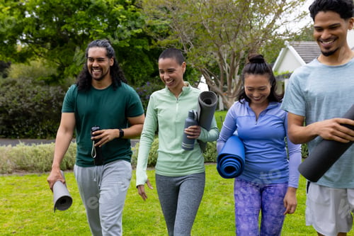 Preview: multiracial friends walking in park carrying yoga mats, smiling and enjoying outdoor exercise
