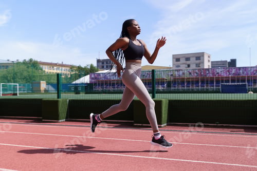 Preview: Fit young black woman in sportswear runs on red track of city stadium preparing for competitions