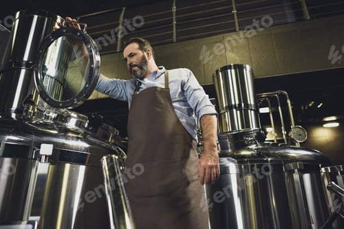 Preview: Male brewer in apron inspecting tank at the brewery